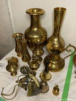 Full view of brass vases, pitcher, bells, and decorative items on white surface.