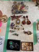 Overview photo showing collection of vintage brooches, rings, earrings, and hair clips in various designs and colors placed on a table.