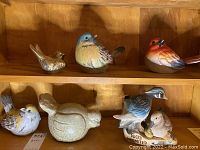 Photo showing three bird figurines on a wooden shelf, including red, blue, and light brown painted ceramic birds, and the Ducks Unlimited Jim Beam decorative bottle.