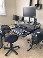 Full view of the black metal frame computer desk with two shelving levels, pull-out keyboard tray, and computer tower tray; black adjustable office chair with mesh back included.