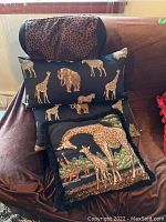 Photo showing all four cushions stacked on a brown fabric surface, includes giraffe, elephant, and leopard print designs on black fabric.