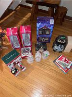 Photo showing full lot of holiday decorations on wood floor including boxed musical house, Fitz and Floyd boxed ceramics, decorative houses, owl figurine, holiday cards.