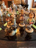 Photo showing three Hummel figurines and one Goebel bird figurine arranged on a glass table.