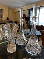 Two identical leaded glass decanters with stoppers and a leaded glass vase shown on a table in a living room. One decanter has a minor chip on the top edge.