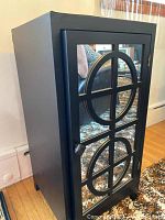 Front and side view of black wooden cabinet with mirrored door and circular geometric overlay