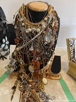 Variety of gold-tone chain necklaces, faux pearls, mixed-metal chains and charm pendants piled on wooden display bust