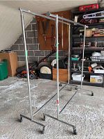 Two metal rolling clothes racks with wheels, showing wear and storage items behind