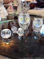 Full grouping of two owls, two small animal figurines and crystal paperweight on reflective surface