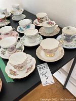 Nine vintage bone china tea cups and saucers arranged on a table showing various floral patterns and gold trims.