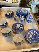 Overview of various blue and white porcelain tea set pieces laid out on paper with multiple small cups, plates, serving dishes, and covered tureen visible.