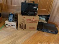 Bell and Howell projector placed on its original box with Wall Movie Editor and box to left and JVC CD player to right on hardwood floor.