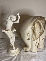 Shows the alabaster ballerina sculpture posed on a marble base and the vintage elephant sculpture with detailed texturing and shape.