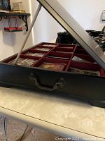 Black wooden tea box with metal handle shown partially open, displaying compartments with tea bags inside