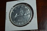 Front side of 1955 Canadian silver dollar coin showing canoe design and inscriptions.