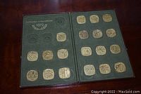 Opened display case showing 16 square commemorative tokens dedicated to 1972 Munich Olympics with various sport and Olympic related images.