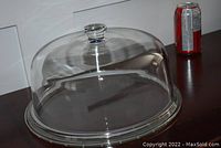 Large clear glass dome with fitted base on a dark wooden surface, soda can for size reference