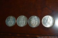 Four Canadian 50 cent coins dated 1964, 1965, 1966, and 1967 placed on a wooden surface showing the coat of arms side.