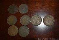 Top view of eight large one cent Canadian coins laid out on a wooden surface showing reverse sides with dates and wreath designs visible.