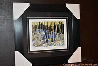 Full view of the professionally framed and matted art print showing the black frame with protective corner covers and visible artwork inside.