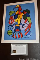 Photo showing full view of colorful "Astral Thunderbird" print with bold outline in red, blue, green, and yellow, along with an accompanying artist profile card below the print.