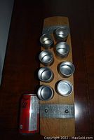 Wine barrel spice rack top view showing curved wood rack with 7 of 8 silver metal spice containers and a soda can for scale.
