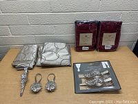 Two sets of matching curtains displayed flat on table with curtain clips and tie backs in front. Light gray patterned pair and burgundy solid color pair visible.