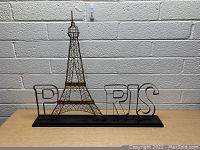 Front view of the large metal Paris sign featuring the Eiffel Tower wireframe in the middle and letters spelling Paris on a black base.