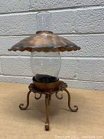 Copper hurricane lamp showing the front view of the glass chimney, copper top, and curled legs base.