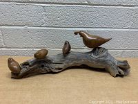 Front angled view of the hand carved wood quail and three small bird sculptures mounted on a textured driftwood base against a pale wall background.