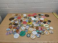 Overview of the large assortment of collectible buttons and pins spread out on a table against a brick wall background.