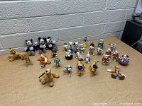 Overhead photo showing 27 assorted Disney character figurines and toys neatly arranged on a table against a brick wall background.