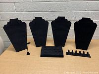 Photo showing seven black velvet jewelry display stands: four bust shapes for necklaces, one smaller bust, one horizontal ring holder with slots, one multi-finger ring slot holder, and one bracelet bar stand.