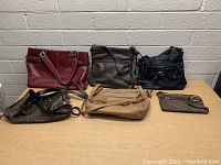 Top view of six assorted purses arranged on a table against a light gray brick wall.