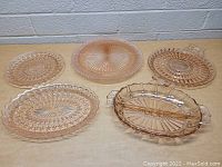 Five vintage pink glass pieces on table showing various round plates and serving dishes.