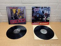 Both vinyl records and album covers side by side on table against brick wall background