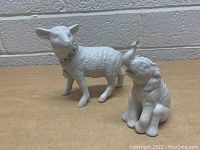 Sheep and elephant figurines in standing and sitting pose on a wooden surface against a brick wall background