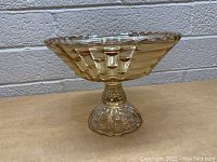 Side view of vintage amber Depression glass pedestal dish showing textured geometric pattern and scalloped edge.