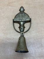 Top view of vintage brass door knocker showing floral and leaf engravings on dome-shaped top and bell-shaped striker