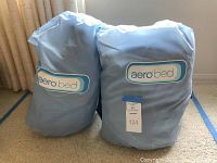 Two packed Aerobed inflatable beds in light blue carry bags with Aerobed logos.