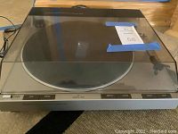 Full view of the Denon turntable system with closed clear dust cover, showing controls on front edge and unit size.