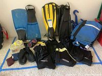 Overview of dive gear including masks, flippers in blue, yellow and black, snorkels, nylon dive suits, diving boots, gear bag, and weights.
