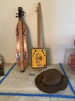 Overview of two dulcimers and leather hat on carpet