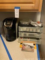 Wide view of the Keurig 2.0 coffee maker with three stacked trays of K-Cups and accessories on a kitchen counter.