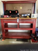 Front view of red Stack-on metal workbench showing pegboard with hooks, drawers, open shelving, and wood top surface with tools and boxes on it