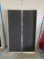 Photo showing full view of two-panel folding ramp with black non-skid surface and metal edges, standing vertically.