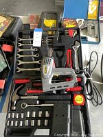 Full view of electric stapler and assorted hand tools in black molded case with sockets, wrenches, pliers, hammer, utility knife, measuring tape