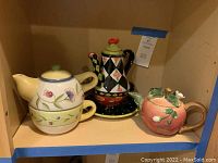 Three assorted decorative teapots placed on a shelf with visible designs and colors