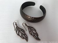 Photo of the burnished hammered bronze cuff bracelet alongside the openwork leaf bronze earrings on a white background.