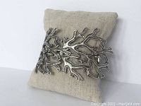 Front view of silver-tone bracelet with intricate branch details displayed on a cushion.