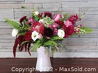Sample arrangement of pink protea, burgundy carnations, white lisianthus, red amaranth and foliage in white vase against stone wall